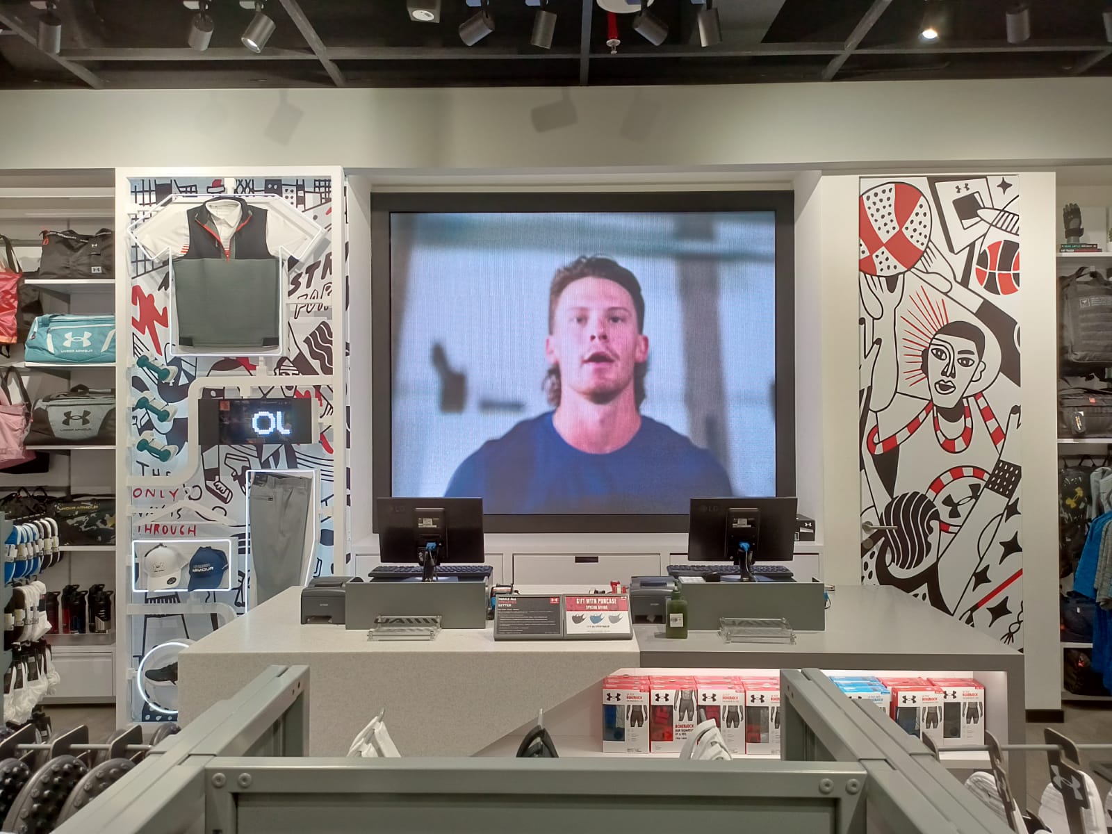 Digital LED screen behind cashier counter at Under Armour Jakarta, featuring dynamic athletic content and modern retail visual merchandising, installed in 2025